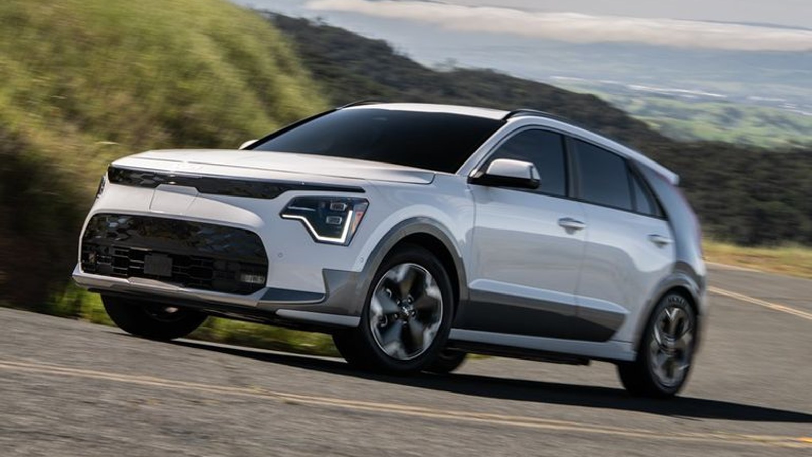 White 2023 Kia Niro EV electric SUV driving on a road.