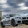 2024 BMW M2 driving on a desert road under a sky filled with thunderclouds.