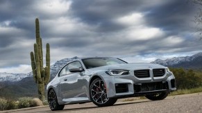 2024 BMW M2 driving on a desert road under a sky filled with thunderclouds.
