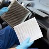 Mechanic with gloves holds up a dirty and a clean cabin air filter.