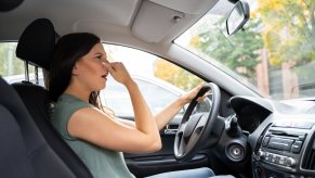 Woman pinches her nose because the interior of her car smells like lettuce after A/C mold
