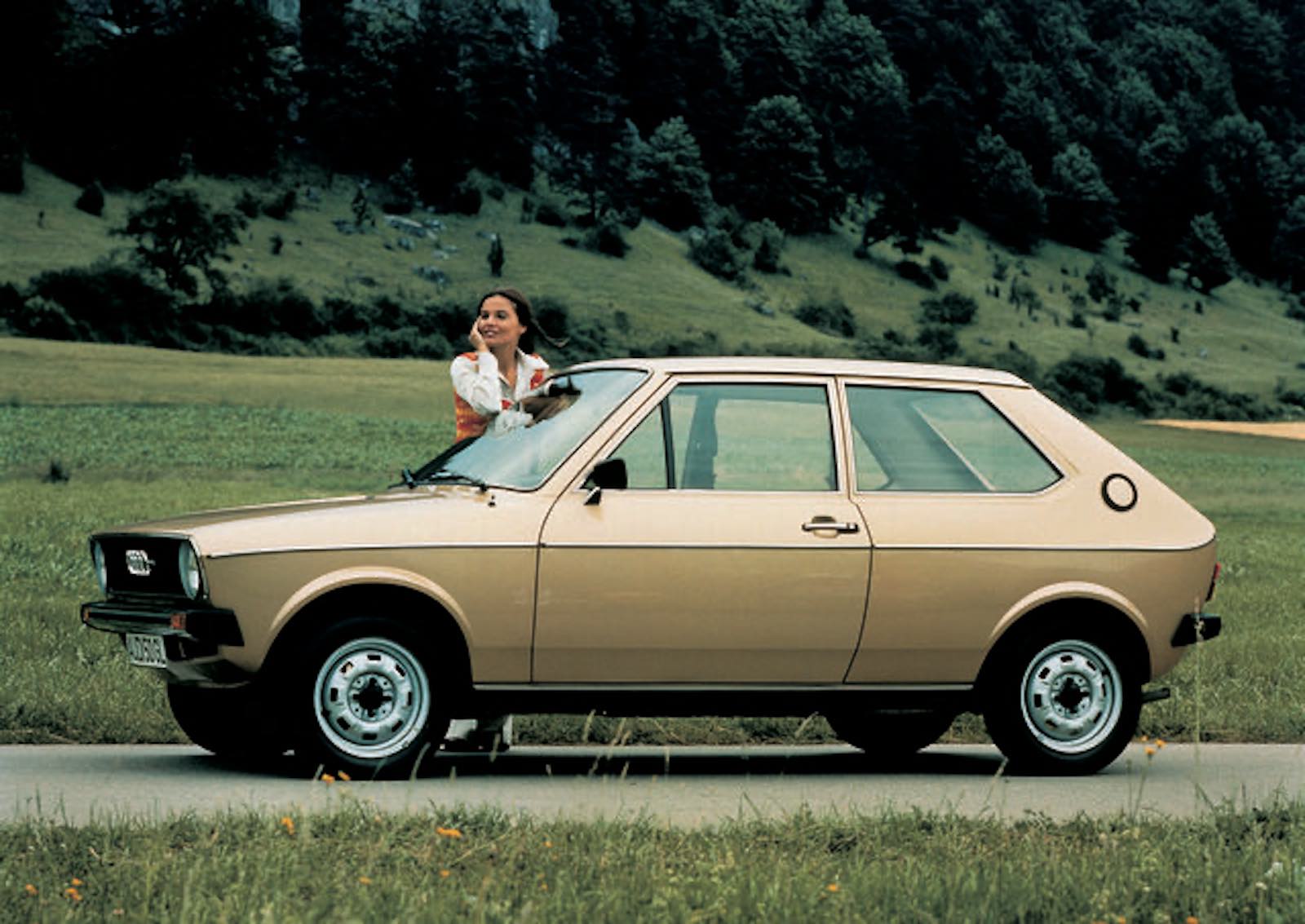 Woman leans on the hood of an Audi car parked in a field.