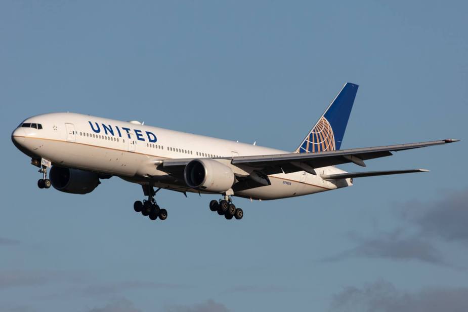 A United Airlines flight, a Boeing 777-200, cruises with its landing gear tires out.