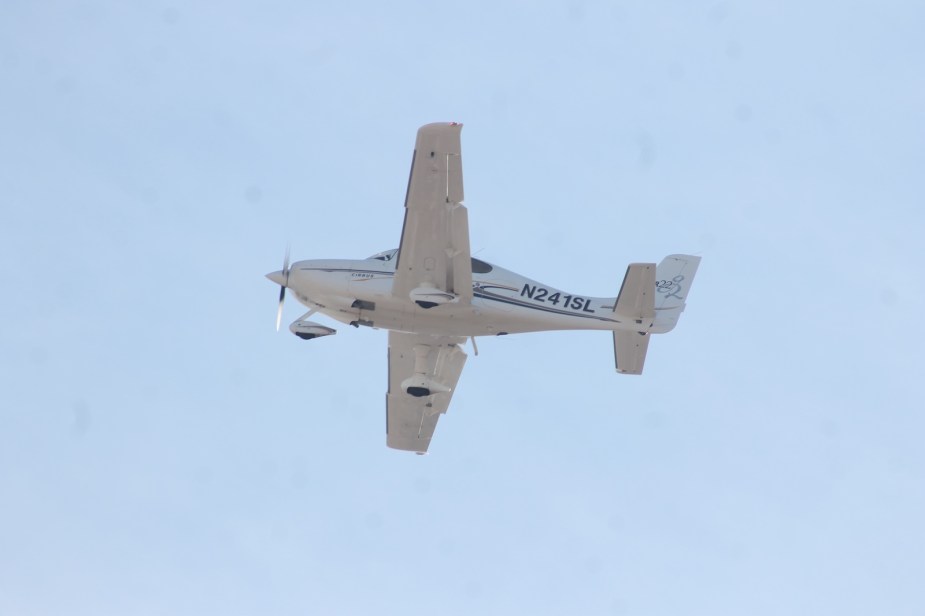 Underside of an ultralight white aircraft against a blue sky.