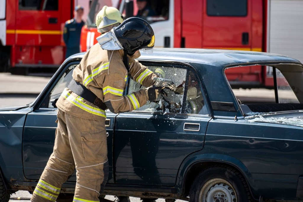A firefighter, not unlike the characters in 'Tacoma FD' and the Lamborghini, breaks a car window.