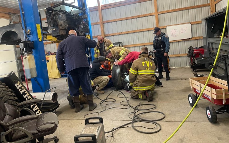 Police and firefighter first responders gathered in an auto shop around a dog trapped in a truck's spare tire rim.