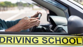 Pointing hand of a man riding along in student driver car.