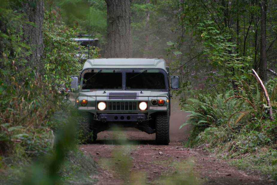 A Humvee in the woods drives with its lights on.