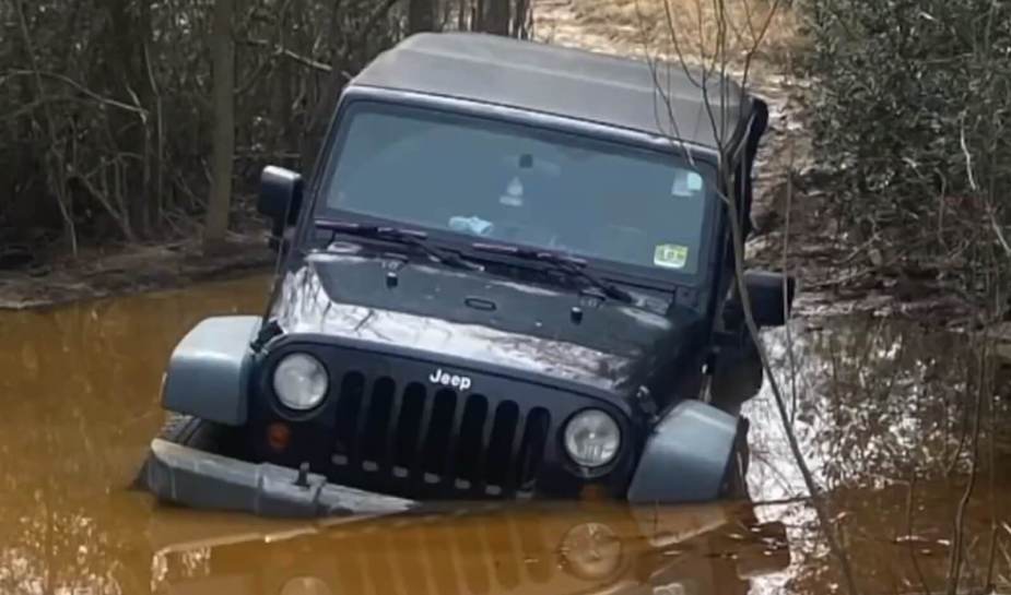 A Jeep Wrangler JK stuck in a boggy trail.