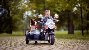 A young child rides a motorcycle toy with a canine passenger.