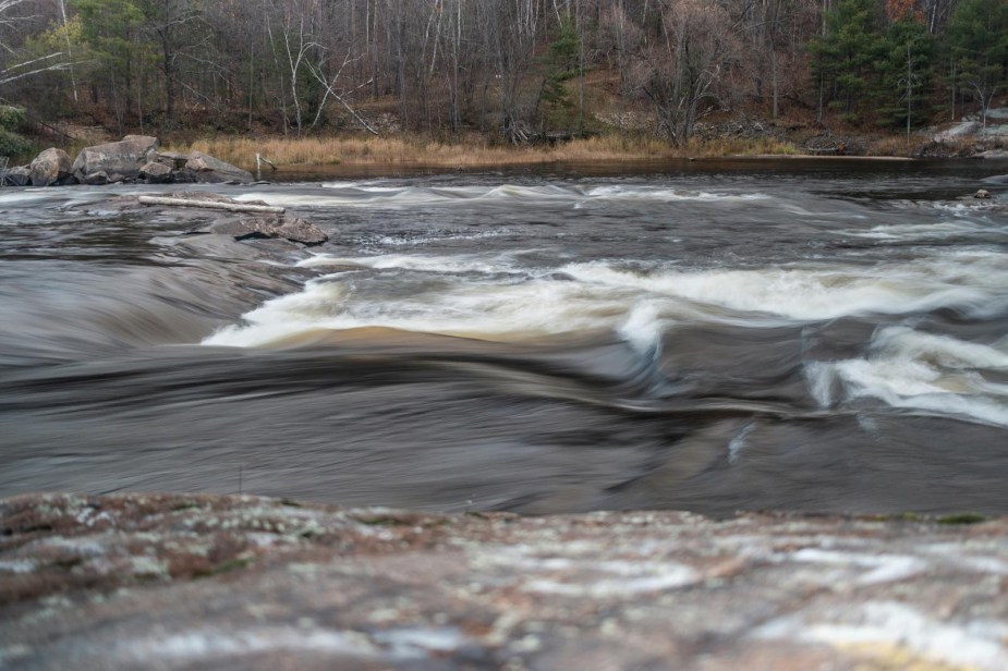 The white rapids of a raging river, bedrock visible in the foreground.