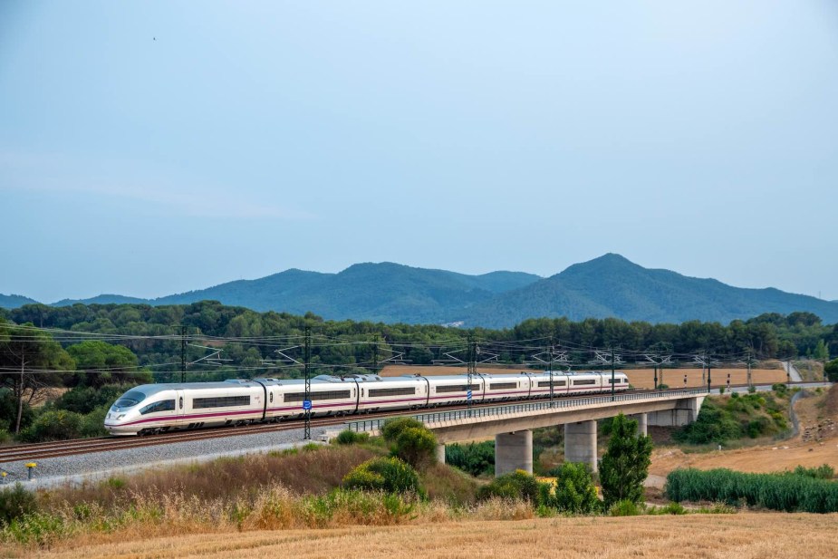 A high-speed rail train races over viaducts, mountains visible in the background.