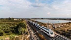 High speed rail train in the countryside, a lake visible behind the tracks.