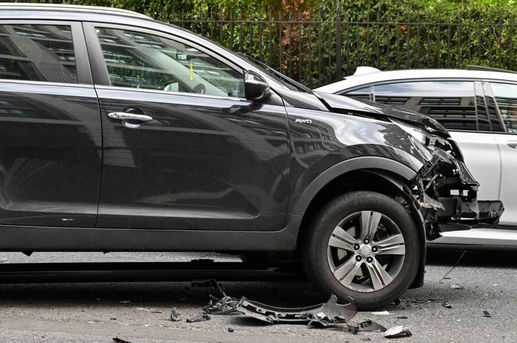 A black SUV is shown center frame in right front side view after a car accident with a white SUV in the background