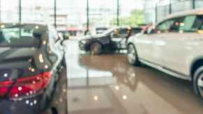 A blurry daylight shot of inside of dealership showroom several cars parked in view