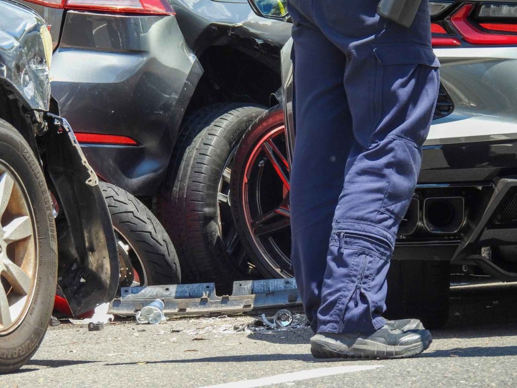 A car crash scene in close view of person standing waist down broken cars and car parts on ground