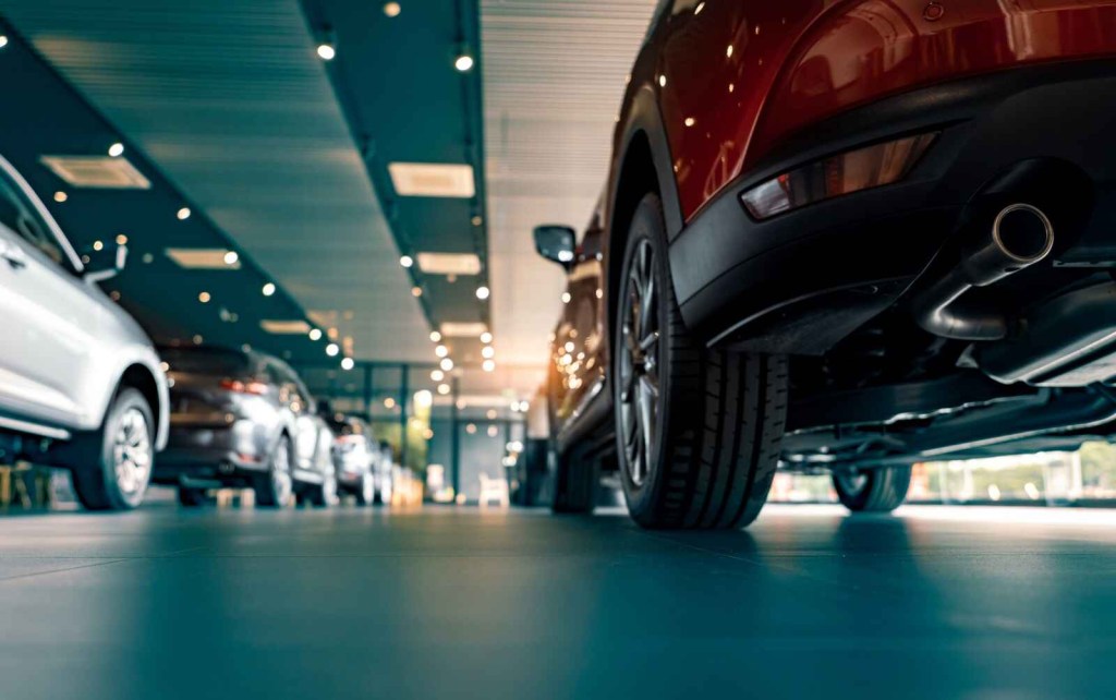 Cars parked inside a dealership showroom in close floor-level view looking up under a dark colored car