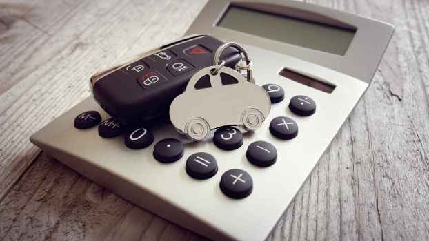 A set of car keys with a silver metal car key chain are set on a pocket calculator on a wood surface