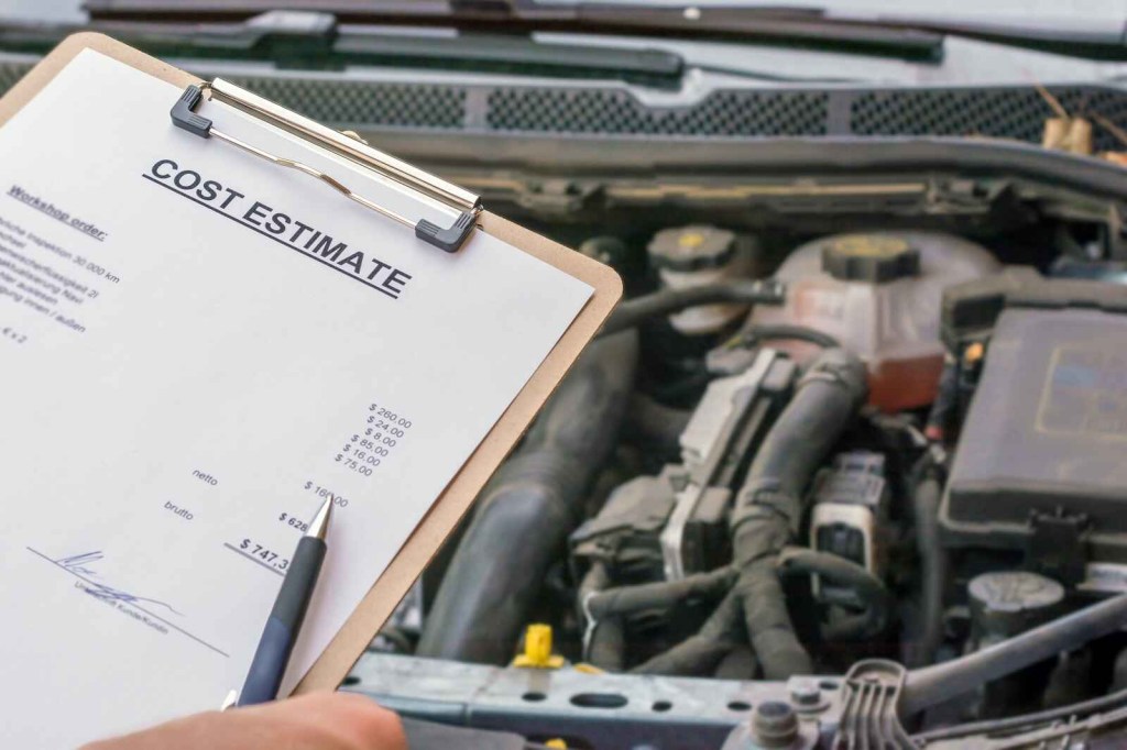 A clipboard being held up with a car repair cost estimate in front of an open car engine hood