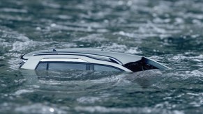 A silver SUV is almost fully submerged in water in right profile view