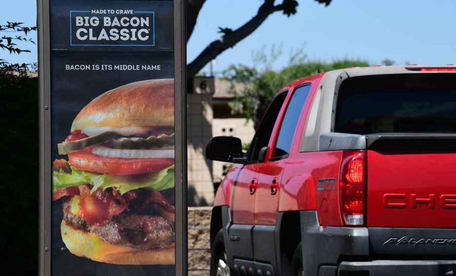 A red Chevrolet Avalanche truck stopped in a Wendy's drive-thru lane next to a large marketing sign for a bacon cheeseburger