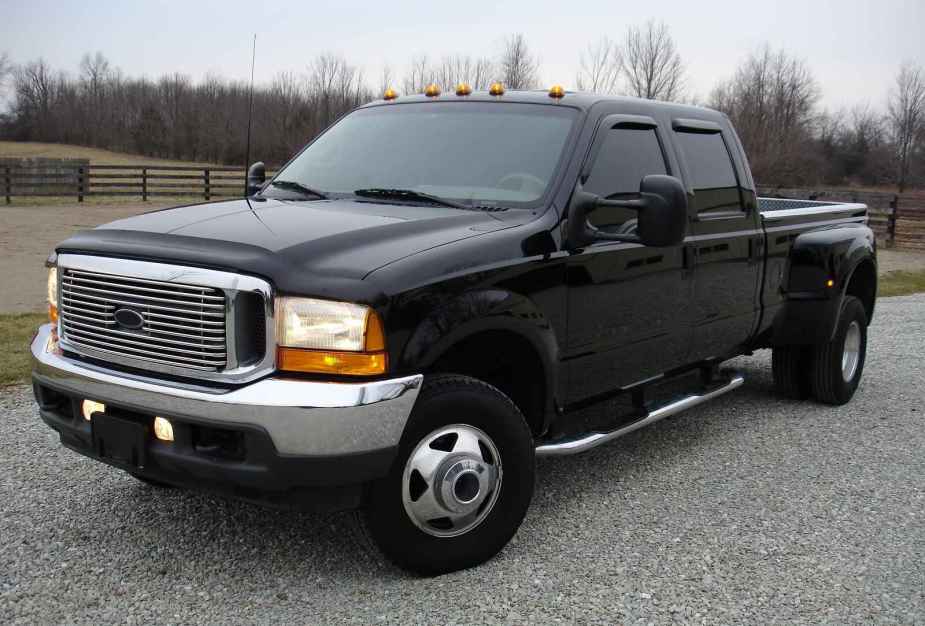 A black diesel pickup truck with dual rear wheels parked on gravel in left front angle view