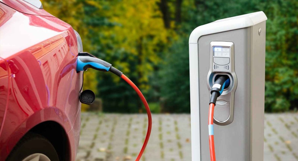 A red EV shown in close left rear profile at a charging station outside plugged in