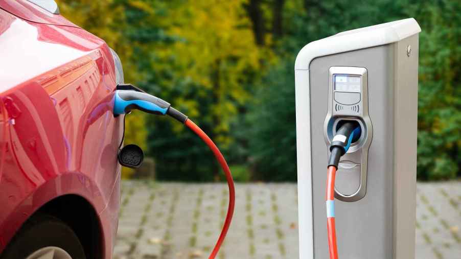 A red EV shown in close left rear profile at a charging station outside plugged in