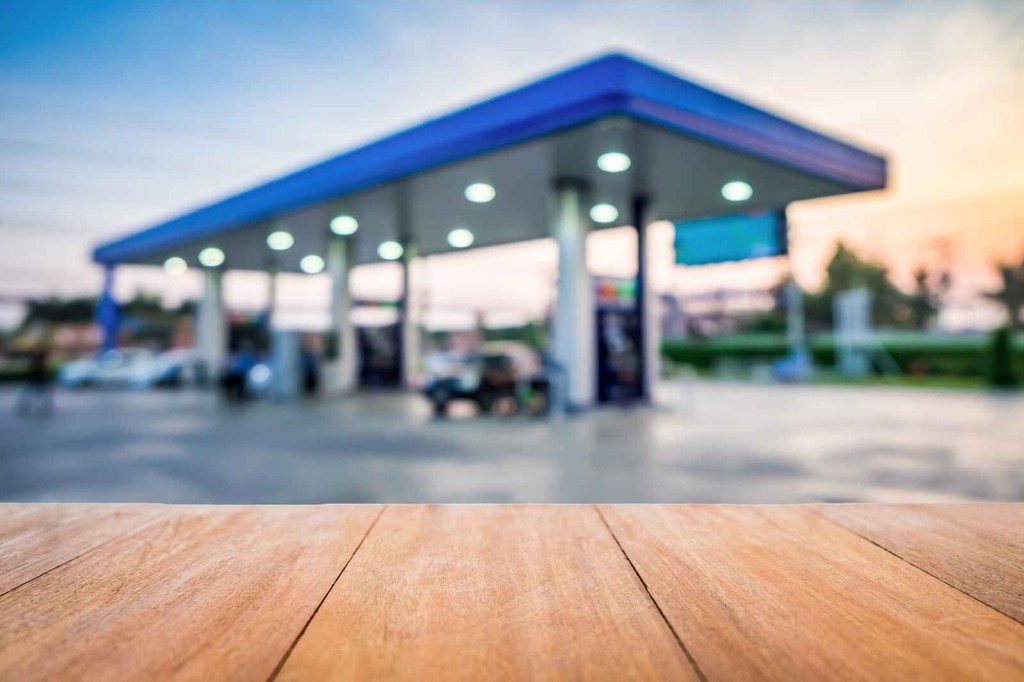 A set of gas station pumps shown in a blurred background wood planks in foreground blue roof on pump building at sunrise
