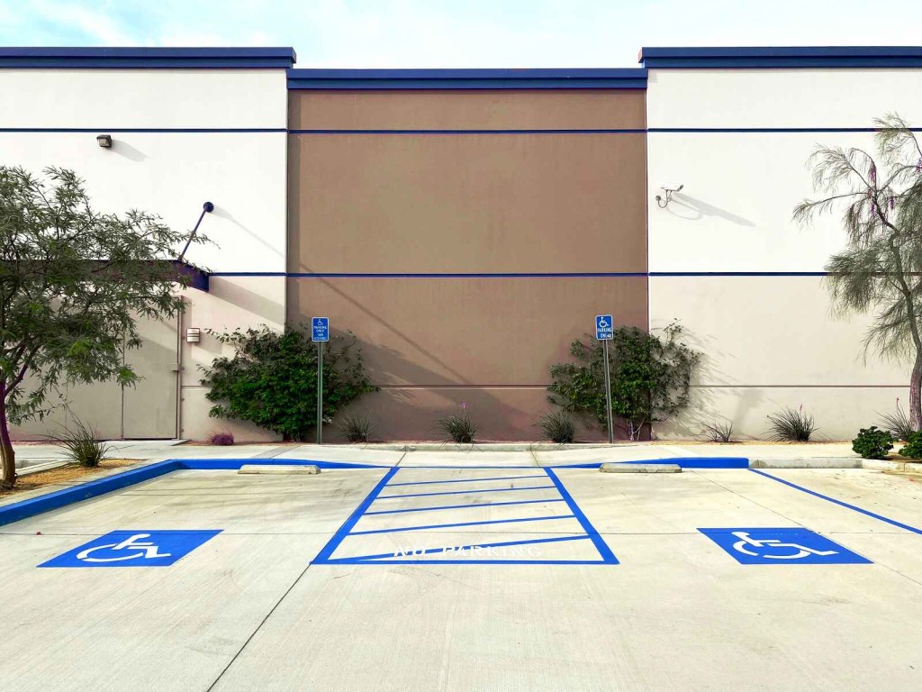 Two handicapped parking spots with blue handicapped parking signs in front of a building parking lot