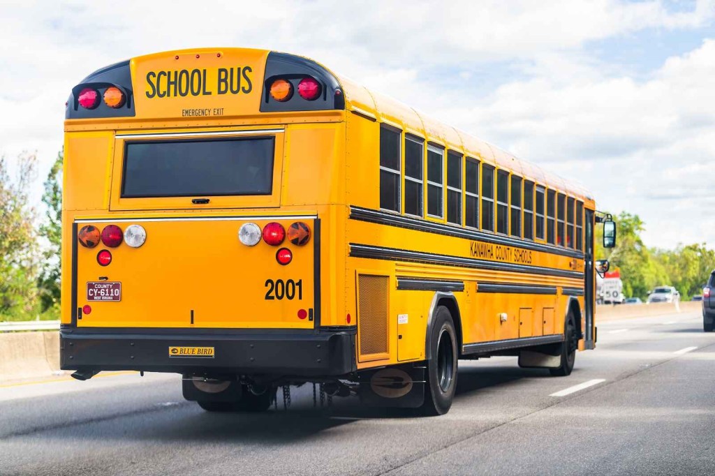 A yellow school bus driving on a paved road traffic in background full right rear angle view