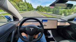 The driver interior view of a Tesla model in self driving mode man's legs under steering wheel no hands