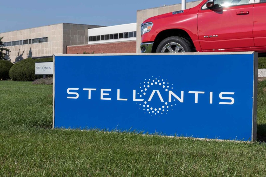 A blue Stellantis sign on a large rectangle in the grass red truck in background