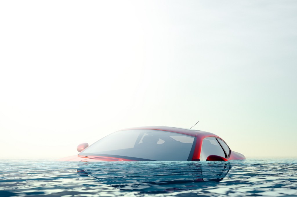 A red coupe is almost fully submerged in water in left front angle view
