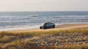 A retendering of a Telo subcompact AWD EV pickup driving down a beach midground right profile view
