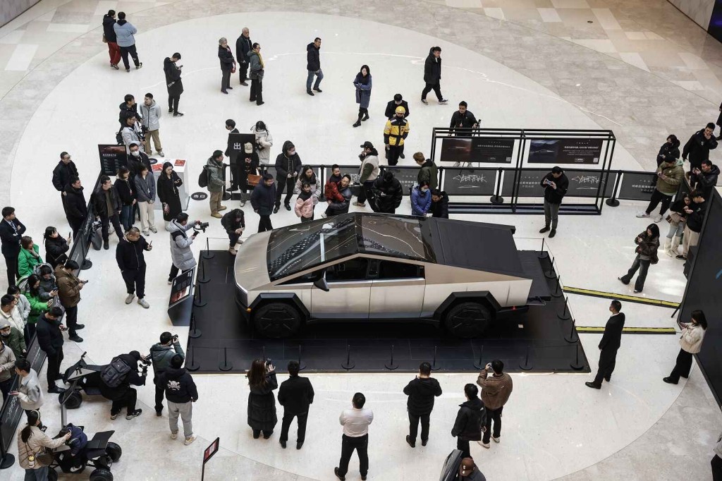 A Tesla Cybertruck on display indoors in China while a couple dozen people look at and photograph the vehicle