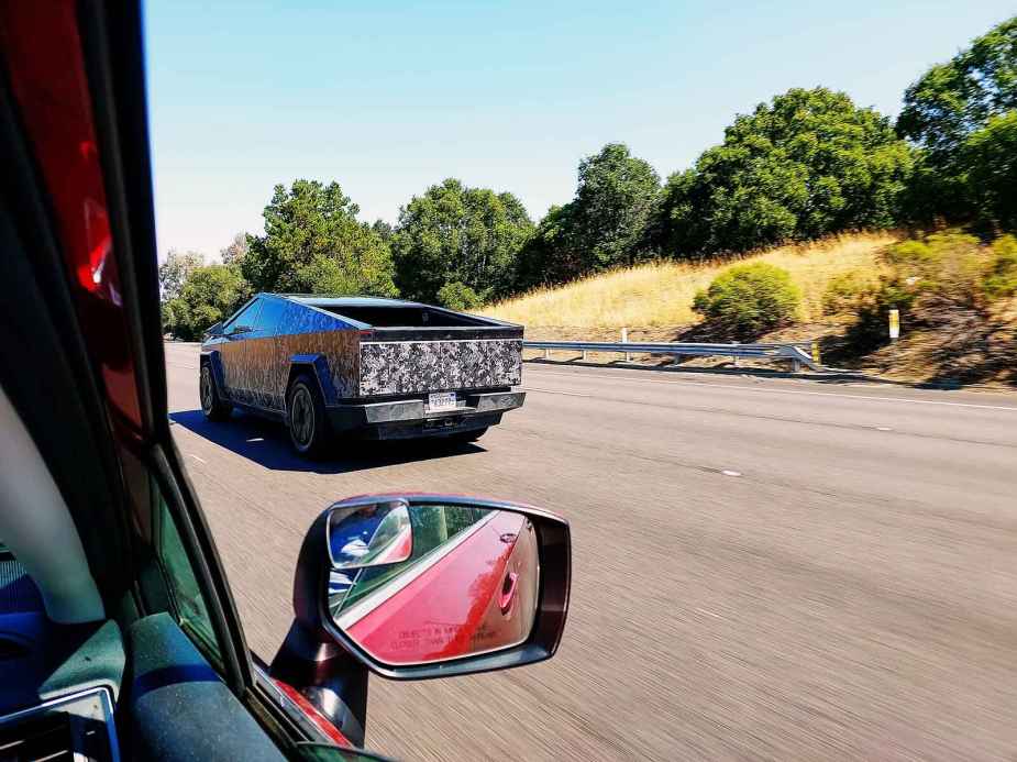 A camouflaged Tesla Cybertruck photographed while driving through a car's passenger front window
