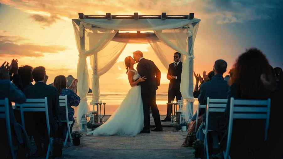 A bride and groom kiss after their beach wedding ceremony sunset