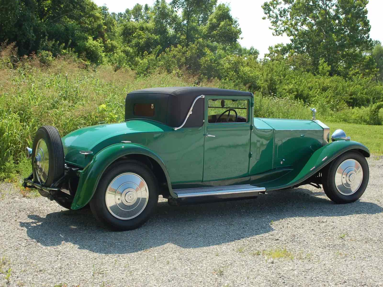 Green 1929 Rolls Royce coupe parked in front of trees.