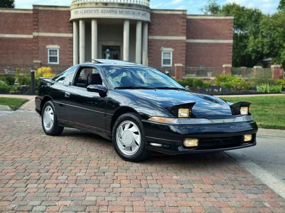 A black 1990 Mitsubishi Eclipse parked at right front angle view on brick path museum of art in background