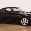 A black 1991 Porsche 911 964 is parked inside a garage floor with white walls in right profile view