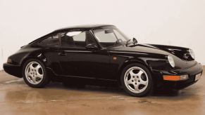 A black 1991 Porsche 911 964 is parked inside a garage floor with white walls in right profile view