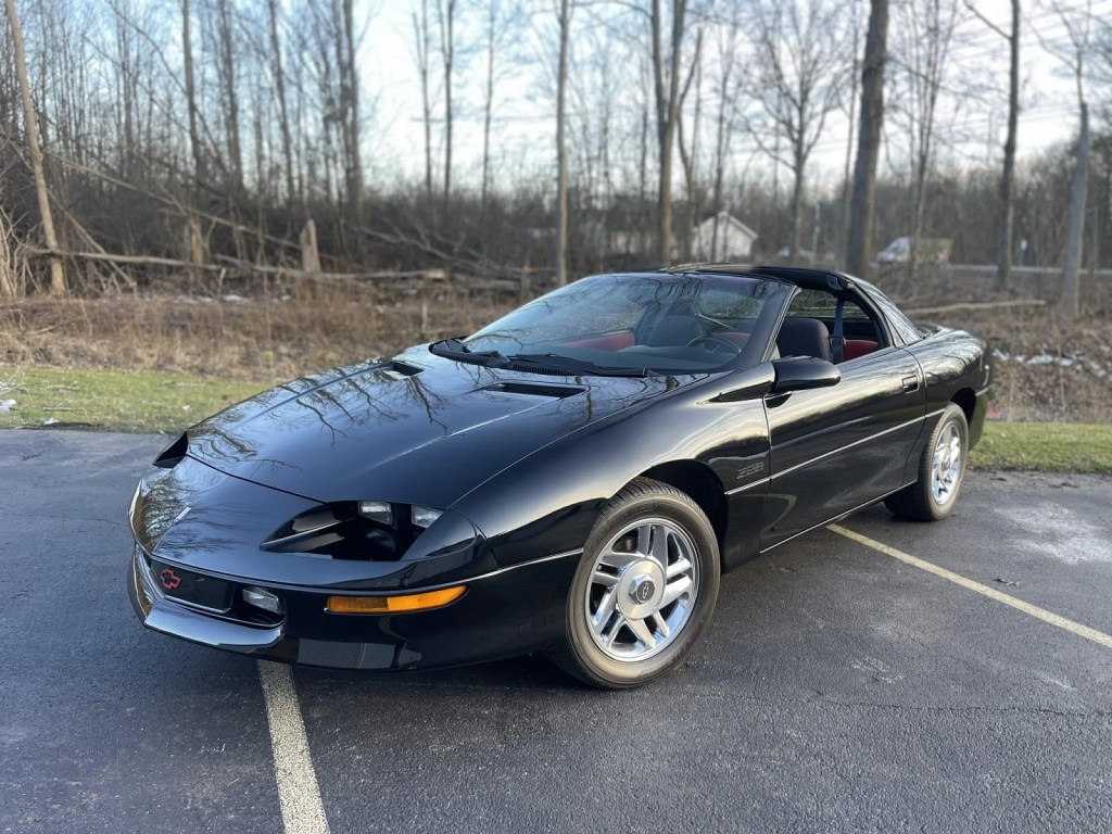 A black 1995 Chevrolet Camaro Z28 parked in a parking lot at left front angle view bare trees in background