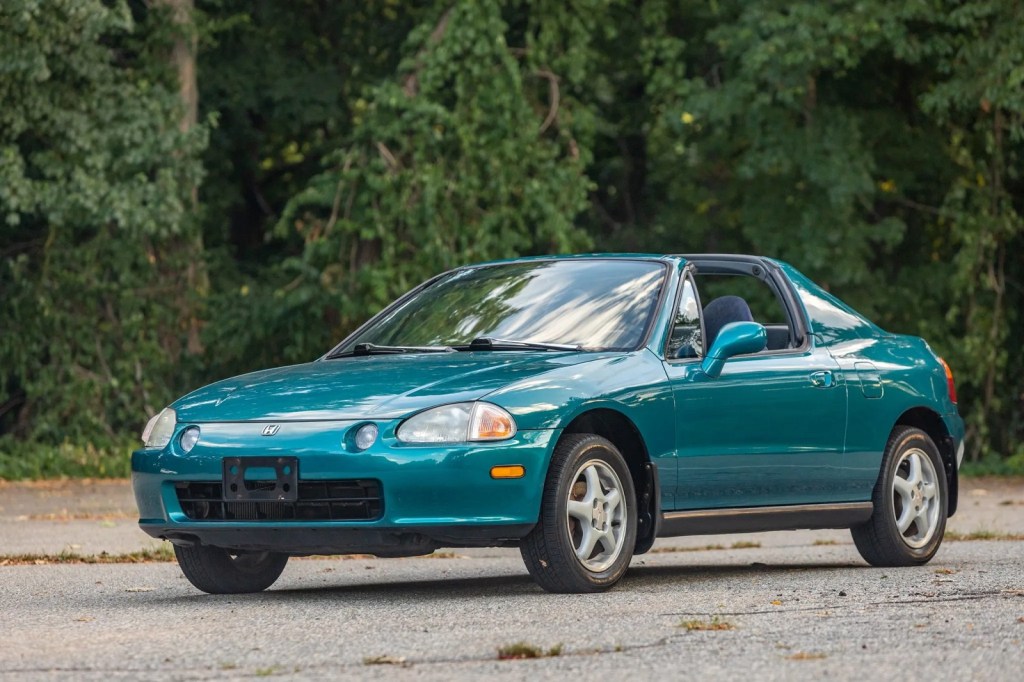 A sea-green 1995 Honda Civic Del Sol parked in left front angle view green trees in background