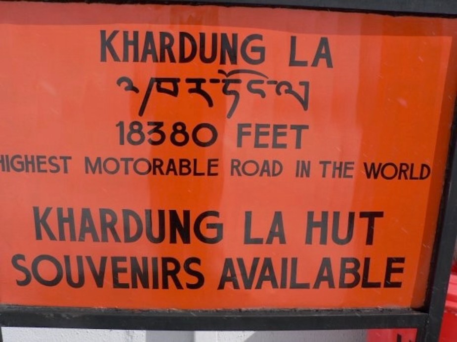 Bright orange sign for the "Khardung La" pass at 18,380 feet.