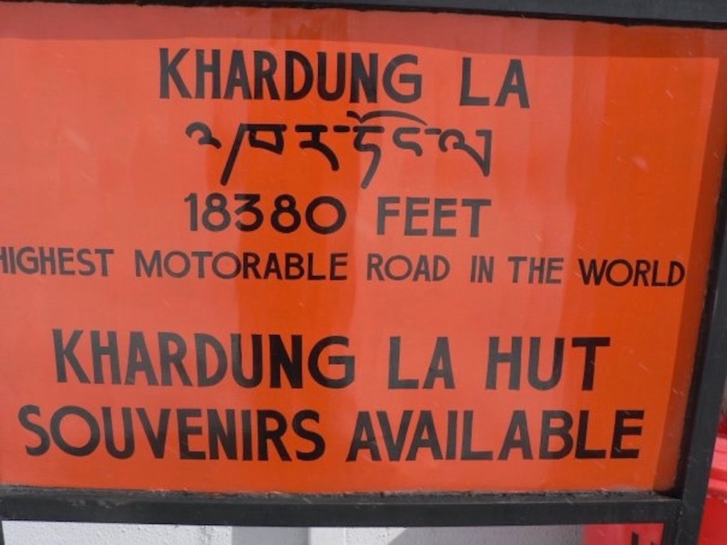Bright orange sign for the "Khardung La" pass at 18,380 feet.