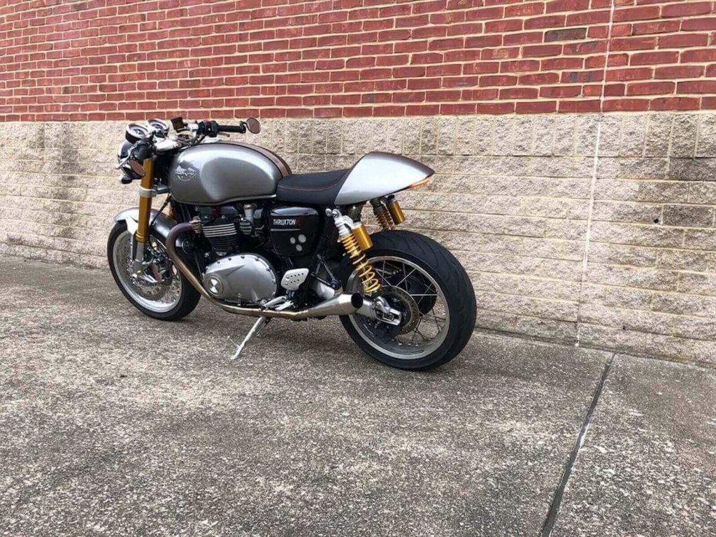 A Triumph Thruxton R parks next to a brick wall. 