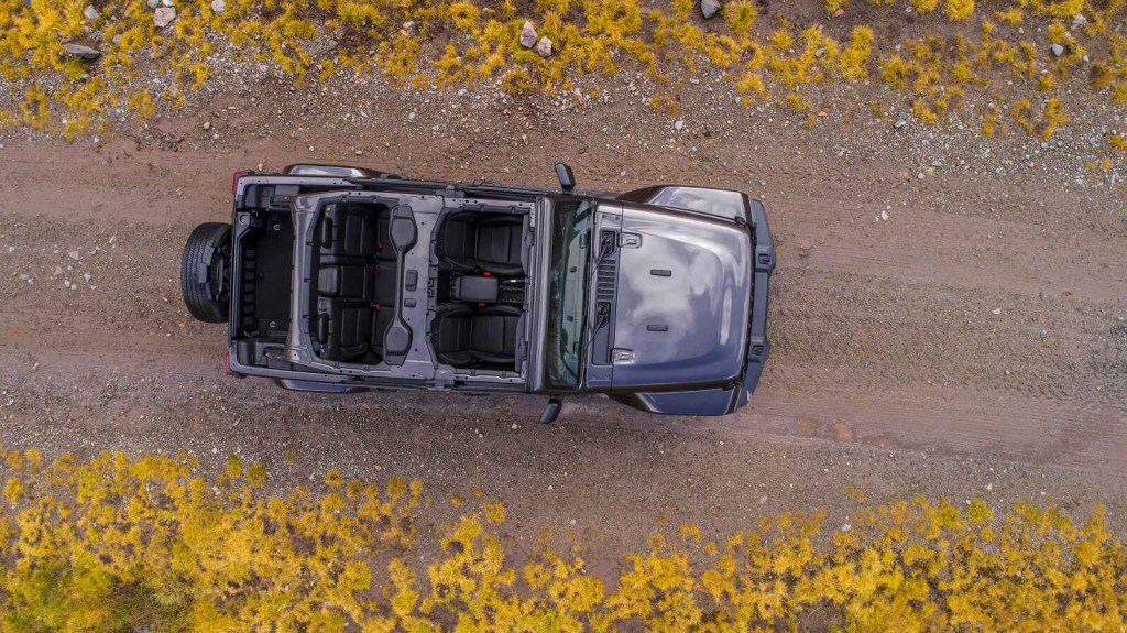 Viewer looking down at a 2020 Jeep Wrangler Sahara drives on a dirt road top view driving facing right frame roof open