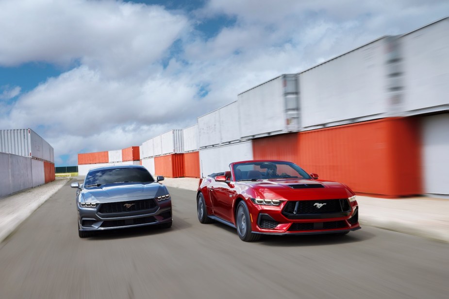 A gray Mustang coupe and red Mustang convertible race along a track.