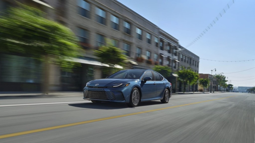 A blue 2025 Toyota Camry XLE sedan cruises down a city street.